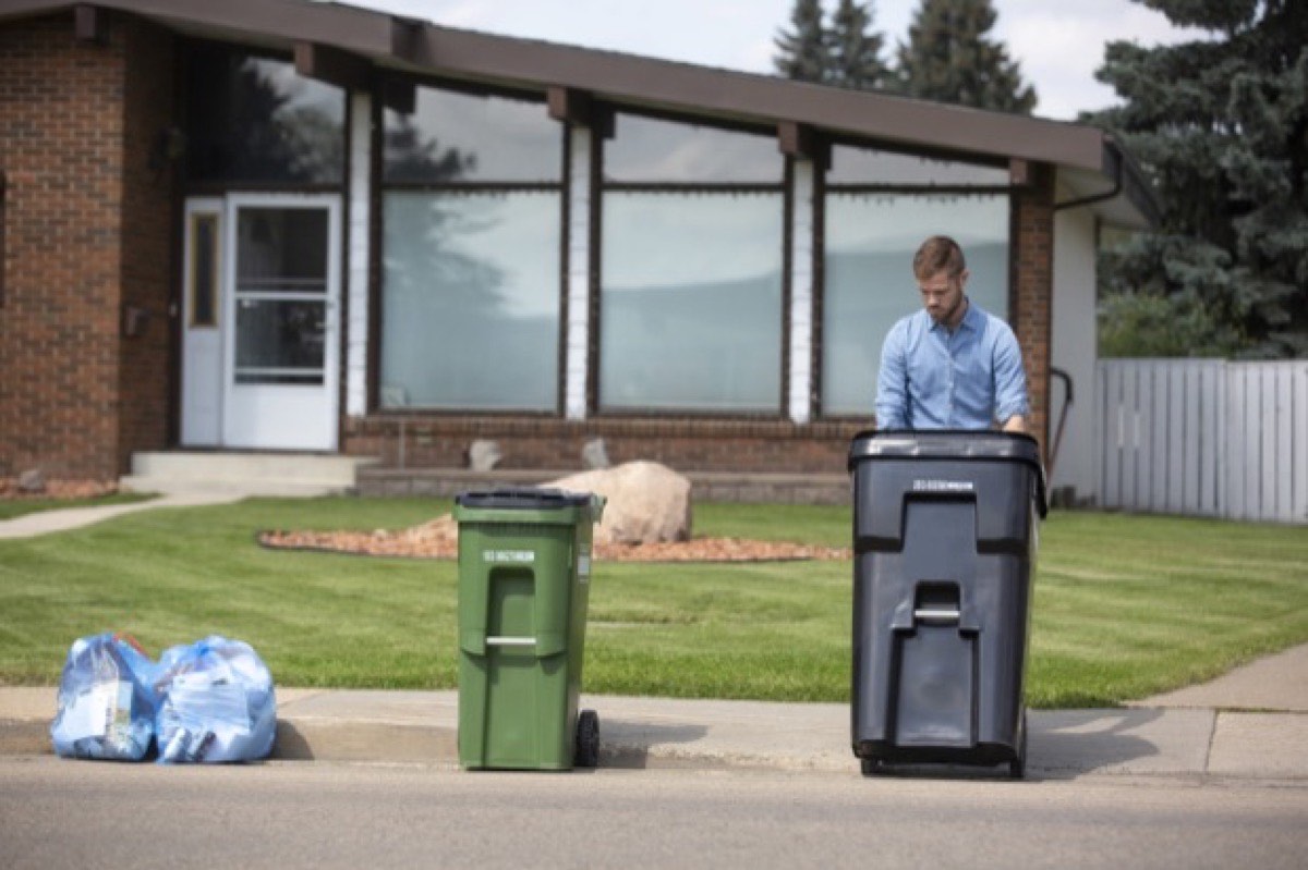 A resident wheeling a cart out to the curb outside a house